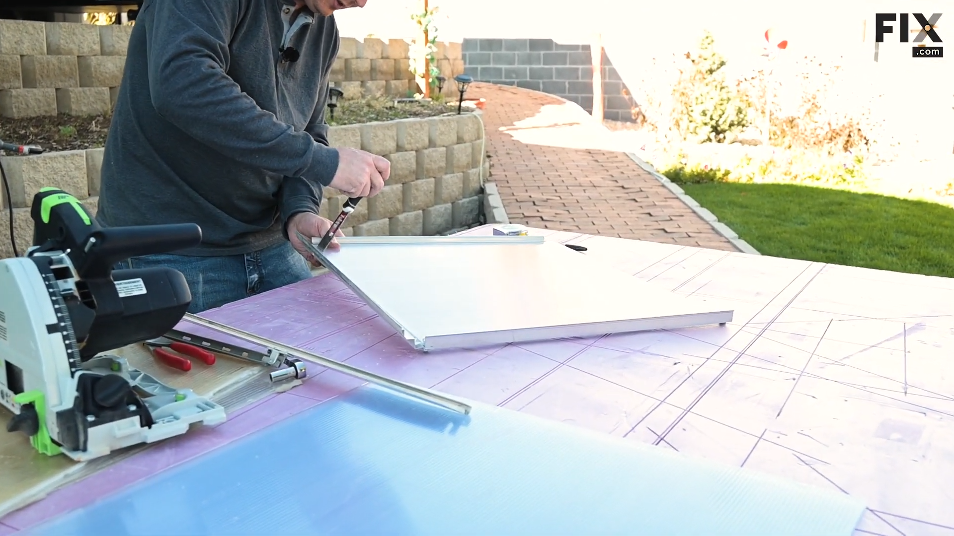 Expert technician fitting a new panel of double-wall polycarbonate into the vent frame of a greenhouse using a putty knife to work it in