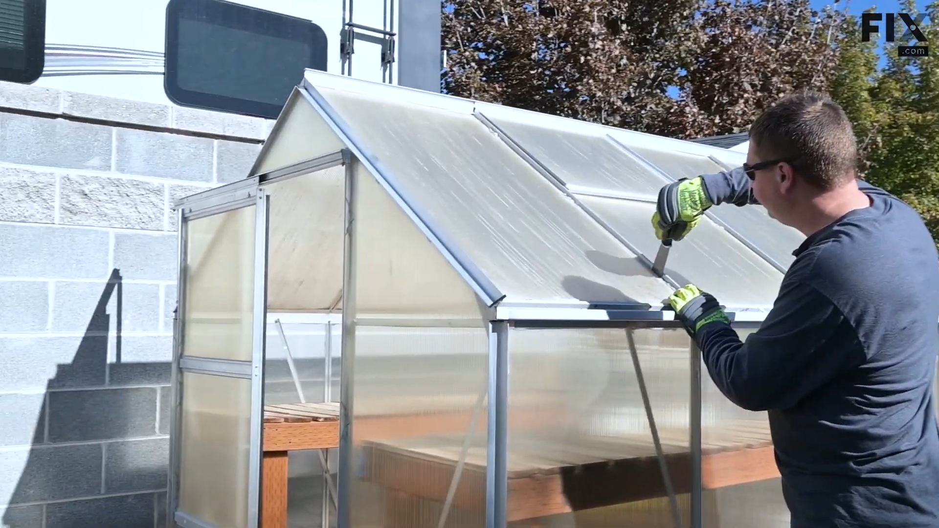 Expert technician using a putty knife to loosen the sides of a roof panel on a greenhouse by slotting the knife in between the panel and the roof frame and wiggling it