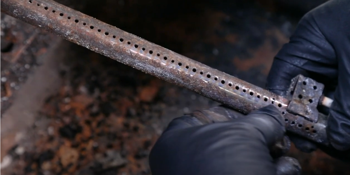 A burner tube from a used grill is inspected for blockages
