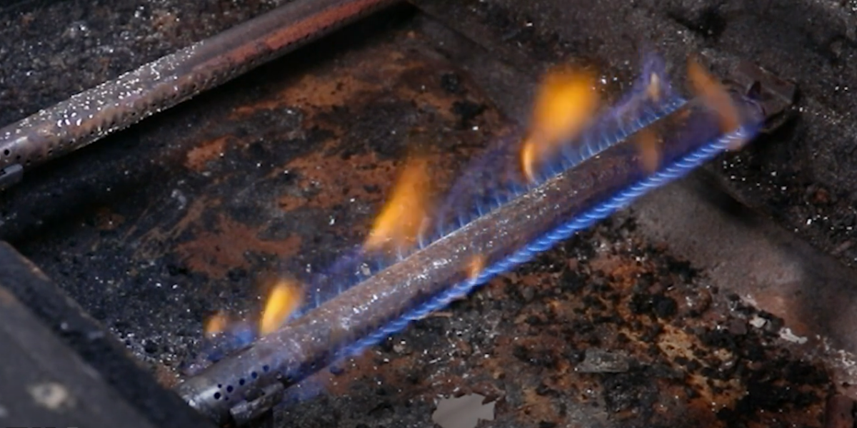 The flame from a grill glows blue with orange tips