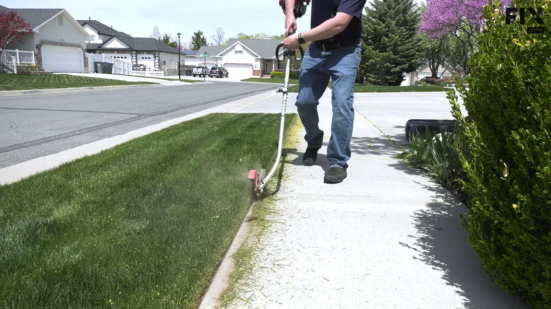 Man in a suburban neighborhood using an edger with a steel blade to trim the edge of a lawn where it meets the sidewalk
