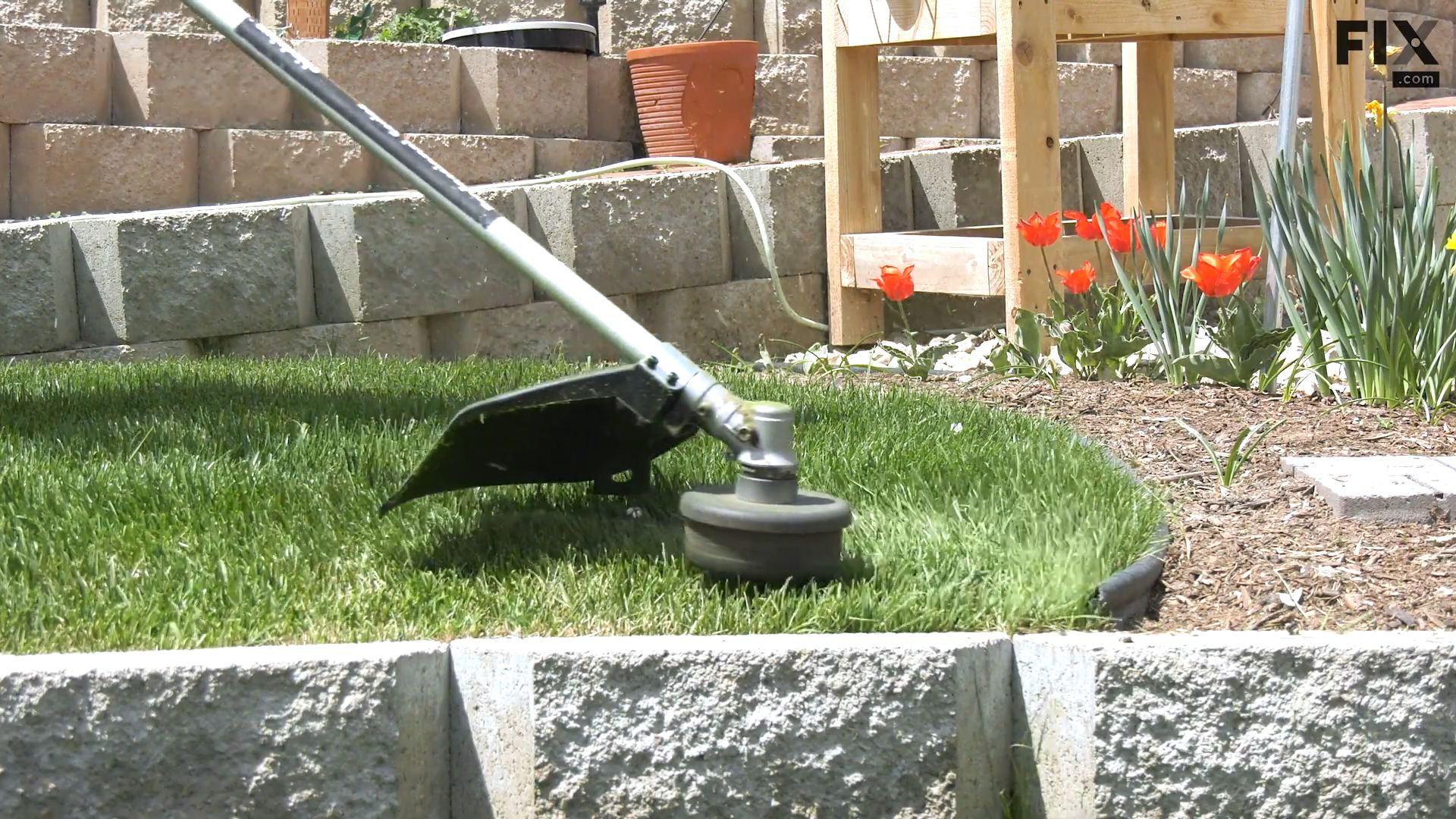 A gas-powered, straight-shaft string trimmer being used to cut grass on a tightly curved section of a backyard garden