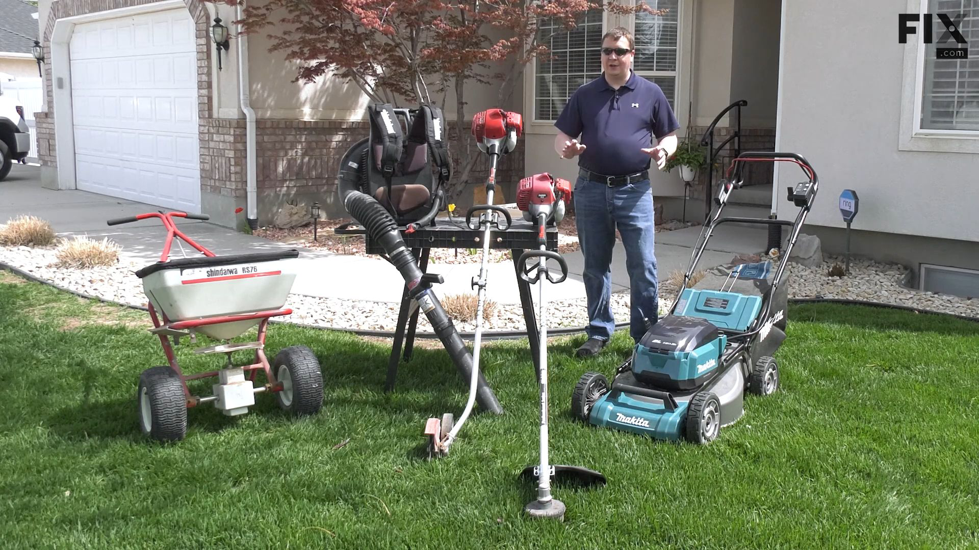 Repair technician standing on a front lawn of a home amongst a lawn mower, edger, trimmer, leaf blower, and fertilizer spreader