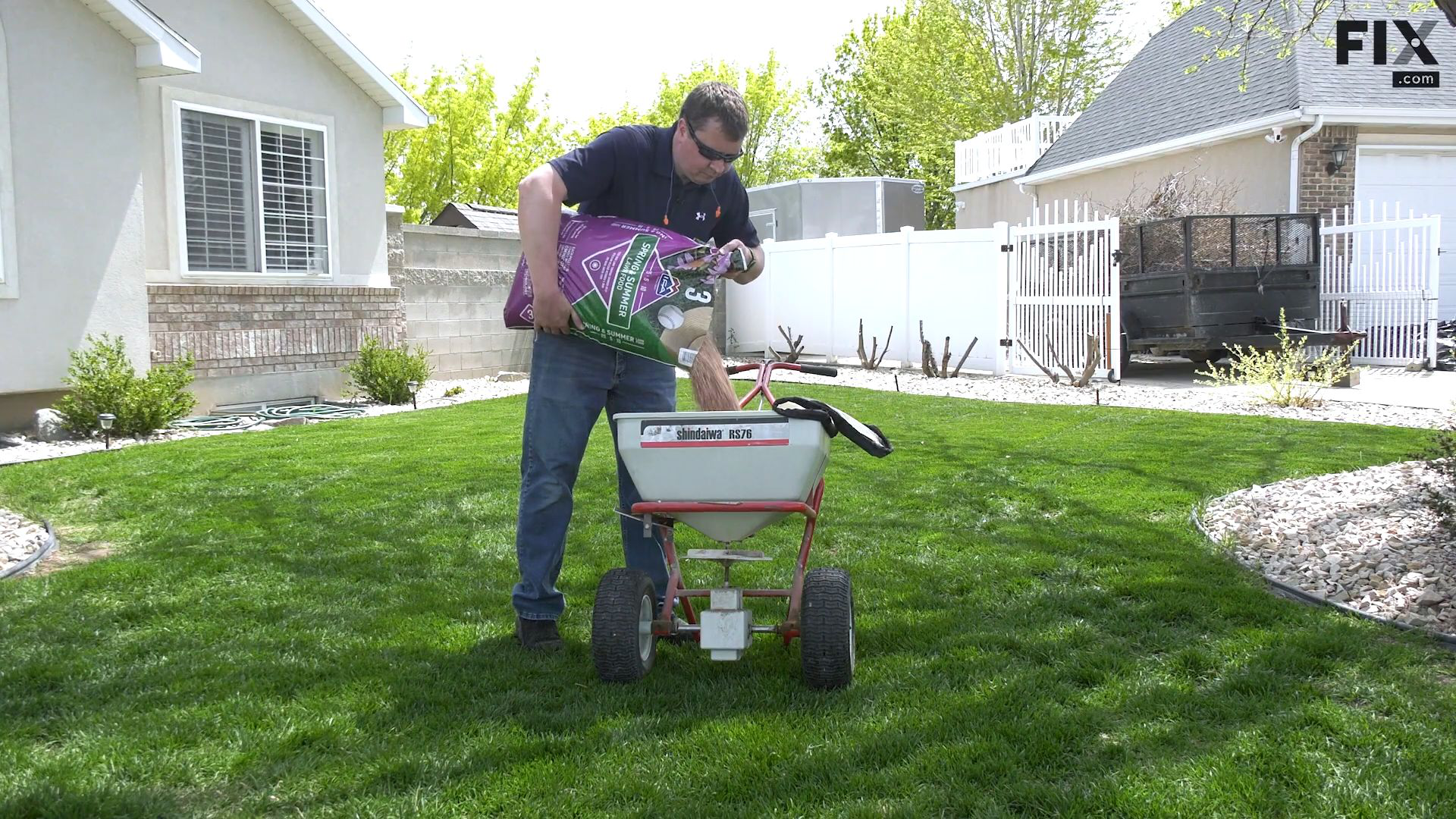 Repair technician standing on a front lawn while emptying a bag of lawn fertilizer to fill up a rotary fertilizer spreader