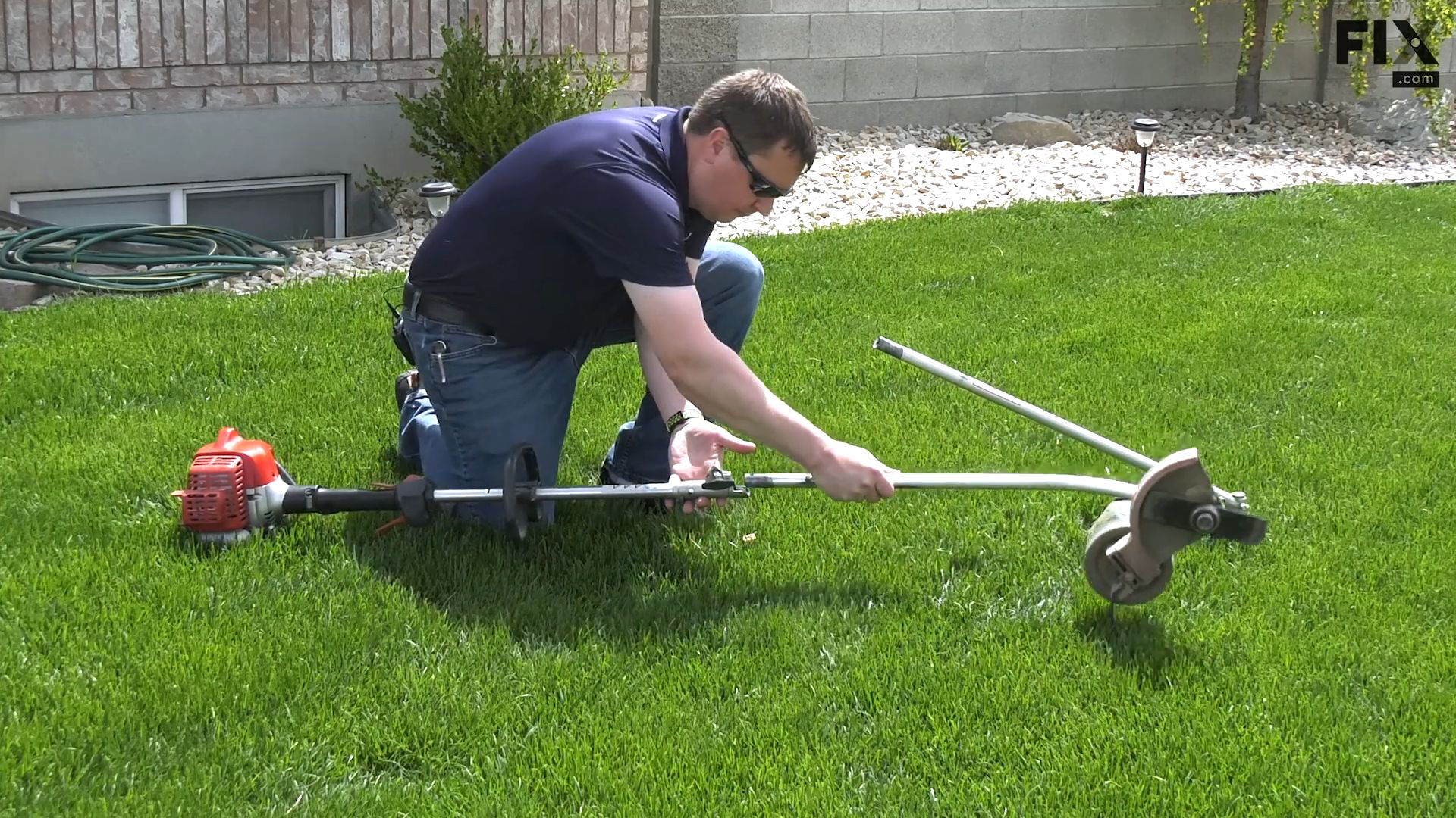 Man on a lawn changing the head attachments on a lawn tool, that uses a split-boom system, from a trimmer head to an edger head
