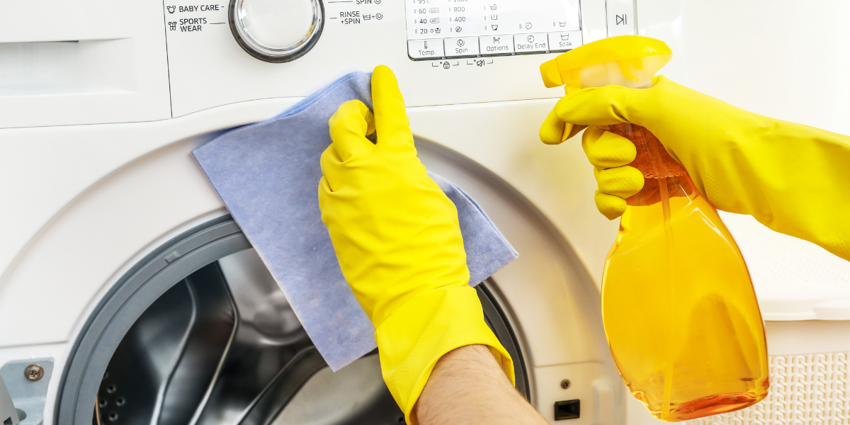 User cleaning the door of a front-loading washer using a pair of rubber gloves, a microfiber towel, and a yellow spray bottle