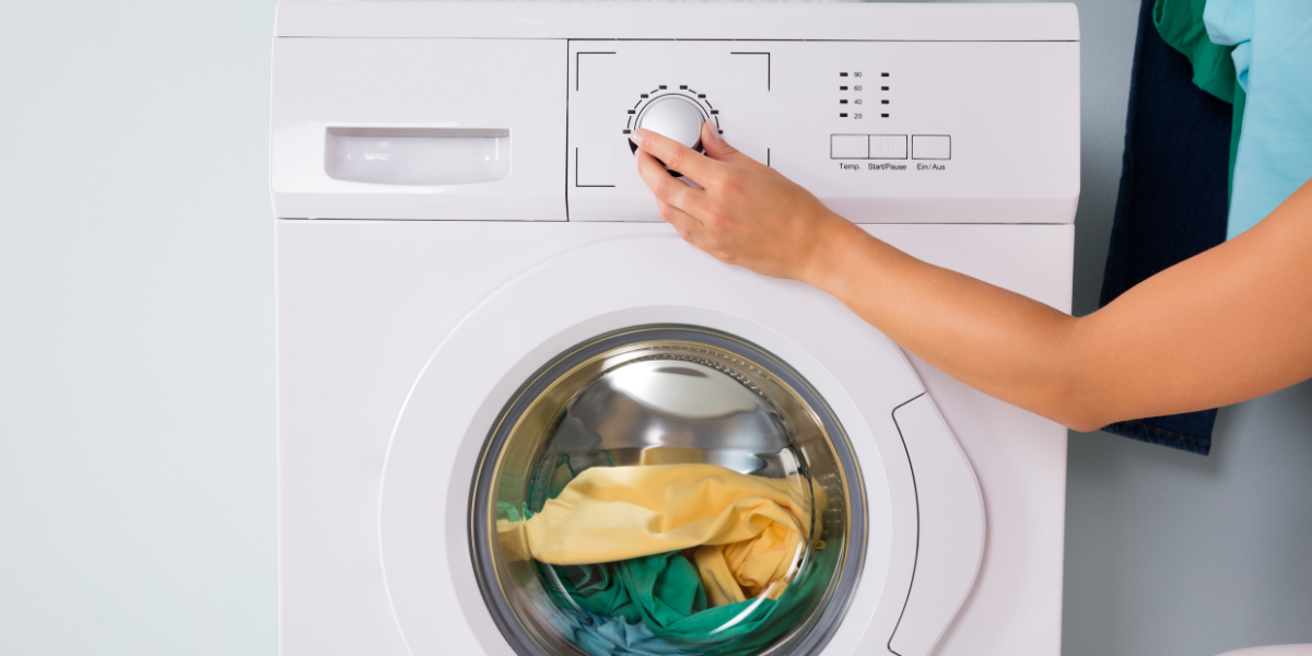 User reaching out and adjusting the dial to select the cycle setting on a loaded washing machine placed in a laundry room.