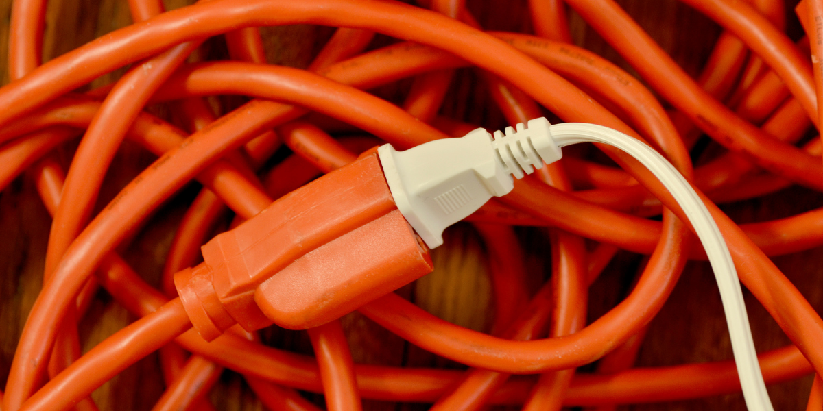A white power cord is plugged into a tangled bright orange extension cord.