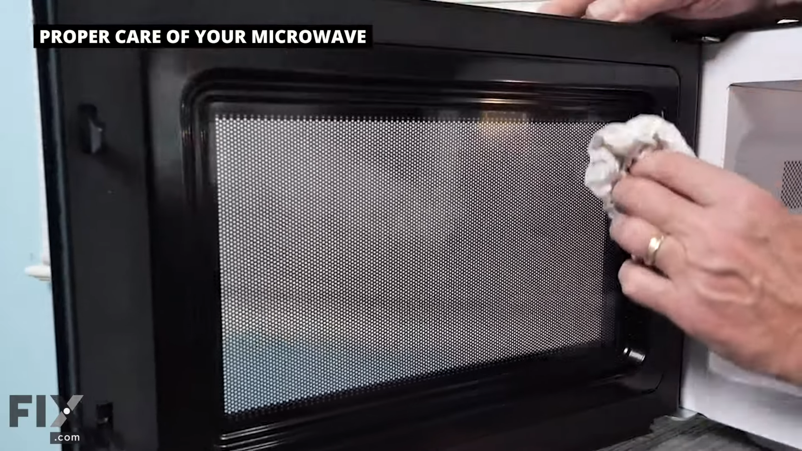 Hand with white cloth cleaning the inside portion of a black microwave door.