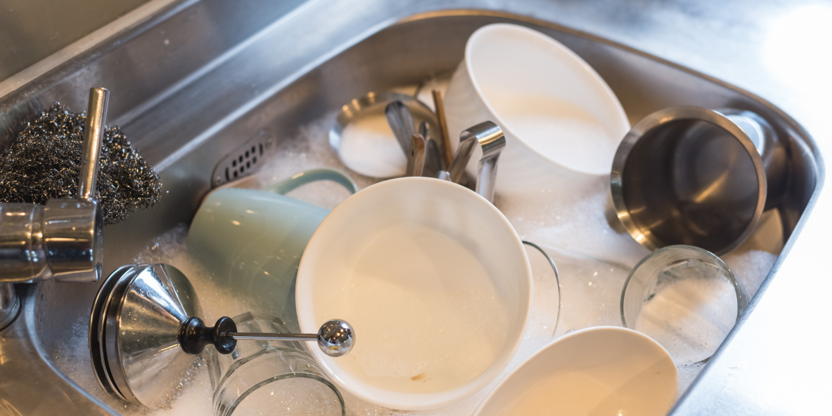 Dirty dishes inside a stainless steel sink filled with soapy water