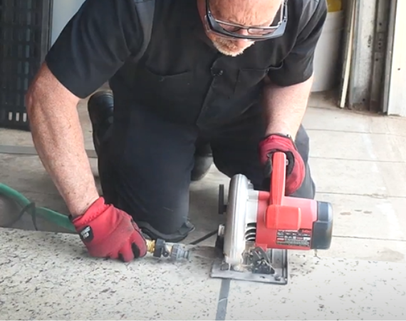 Repair technician sawing through a slab of granite marked by painters tape, using a garden hose and wearing protective gloves