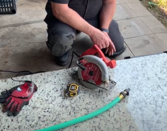 Repair technician setting up to cut granite with supporting weights, protective gloves, measuring tape, hose and circular saw