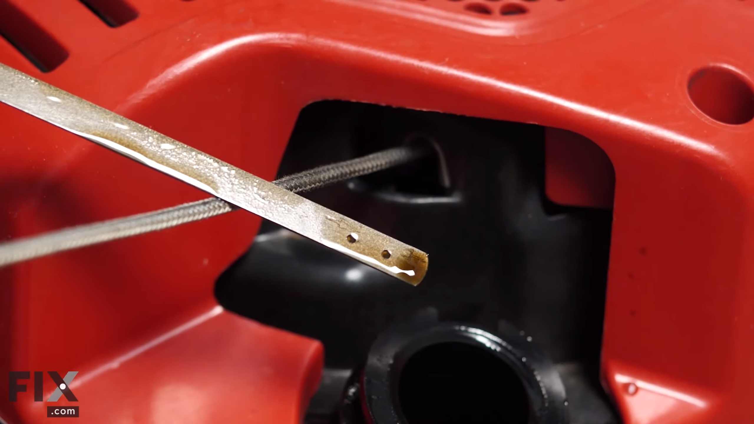 Metal oil dip stick in front of red lawn mower engine