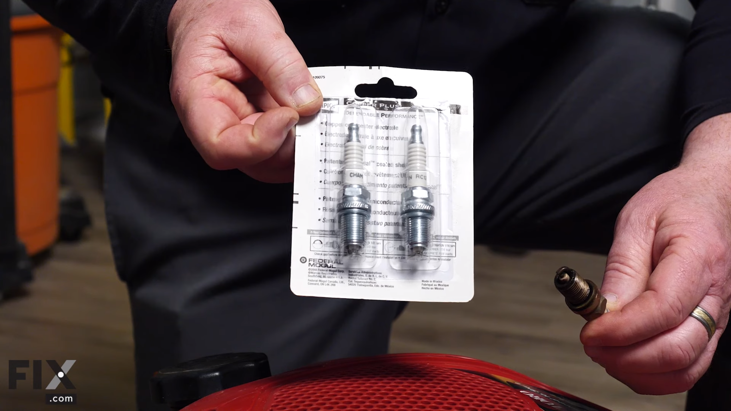 Person holding two spark plugs in white packaging.
