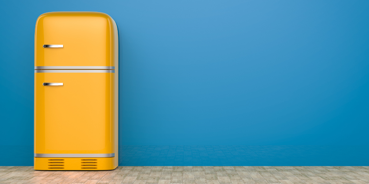 A bright yellow fridge sits in front of a dark blue wall.