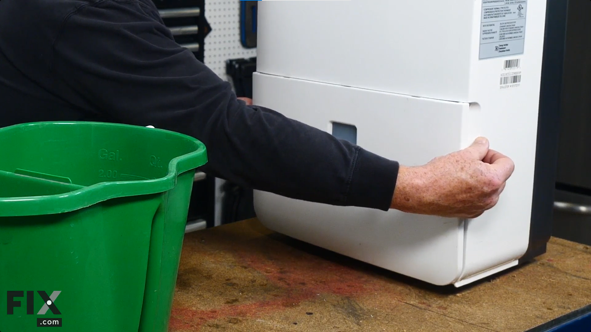 A repair technician pulling the water reservoir out from the bottom of a dehumidifier to empty it into a green bucket.