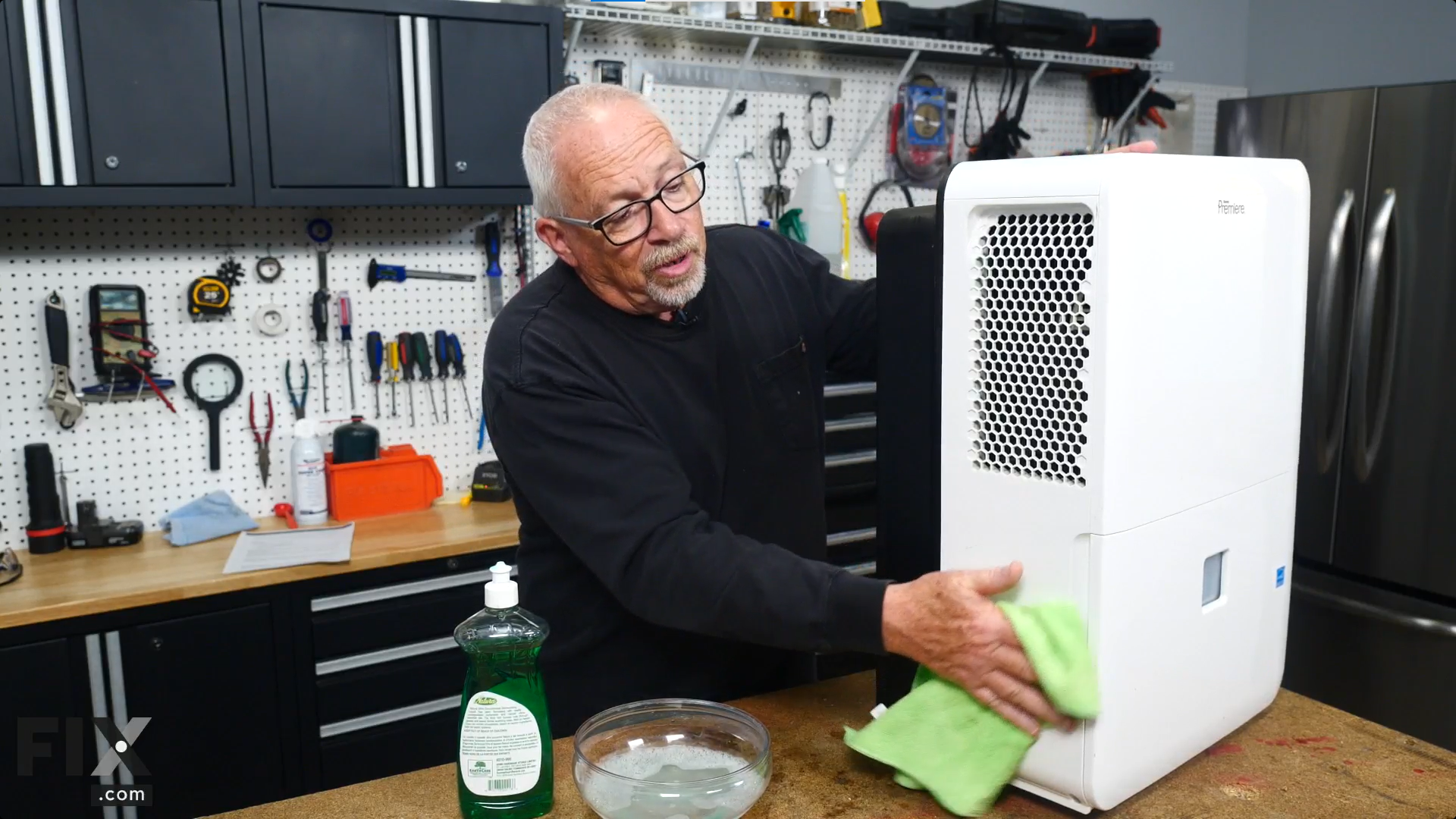 A repair technician, beside a bowl of soapy water, wiping a dehumidifier's plastic casing with a green microfiber cloth.